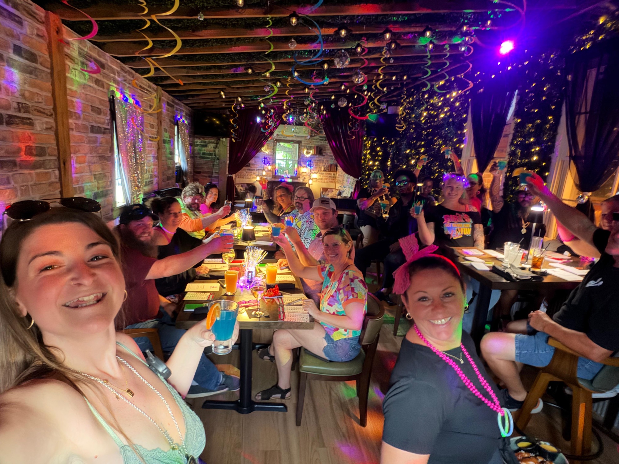 Guests raising a toast at a Murder Mystery Dinner in the string-lit ivy room at The Oak and Ivy Taphouse, Smithfield VA